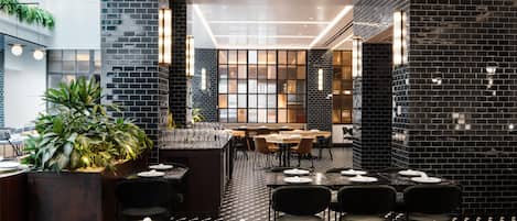 Un restaurante con paredes de baldosas negras, una zona de bar central y diferentes distribuciones de mesas.