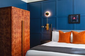Un dormitorio con un armario de madera, una cama con almohadas blancas y anaranjadas, una mesita de noche y un aplique de pared.