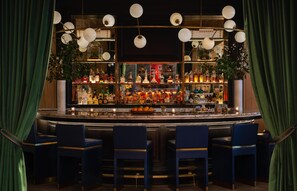 Zona de bar con encimera de mármol, varias botellas de licor y taburetes azules.