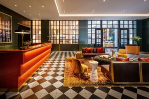 Una hall d'albergo moderna con pavimento a scacchi, una reception, una zona salotto e ampie finestre.