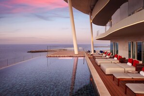 A luxurious infinity pool with a view of the ocean, wooden deck seating, and a modern architectural design. - The St. Regis Al Mouj Muscat Resort (Muscat)