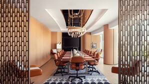 A modern conference room with a long table, orange chairs, and a chandelier.