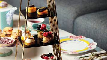 Um suporte escalonado para doces com diversos pastéis e uma chaleira sobre uma mesa.