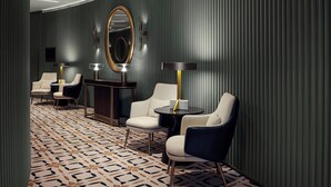 A modern hotel room with a patterned floor, a large mirror, and two seating areas with lamps.