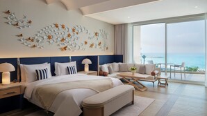 Quarto de hotel moderno com uma cama grande, área de estar com vista para o oceano e parede decorativa com padrões de folhas.