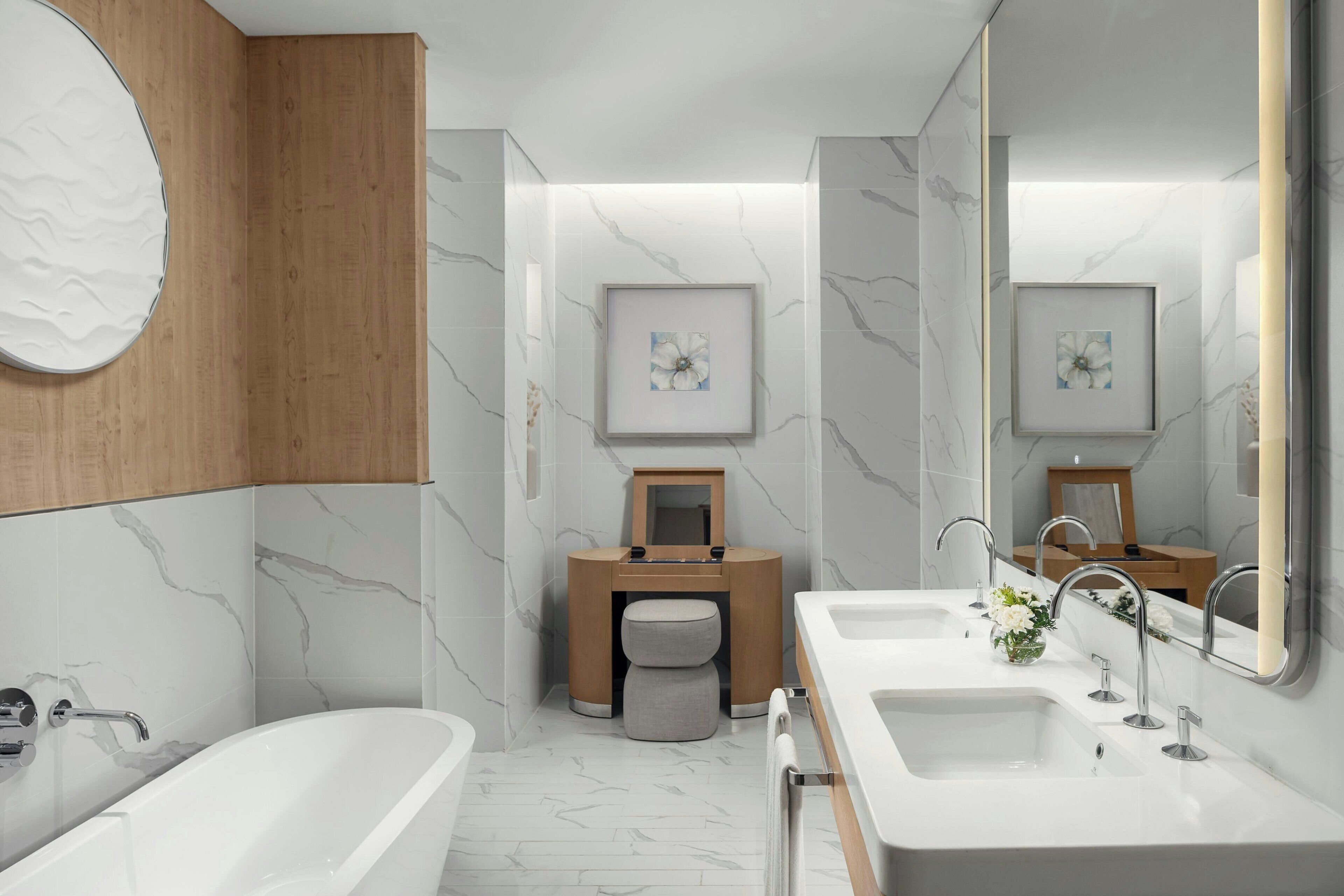 Ein modernes Badezimmer mit einer großen Badewanne, zwei Waschbecken, einem Waschtisch mit Spiegel und gerahmten Bildern an den Wänden.