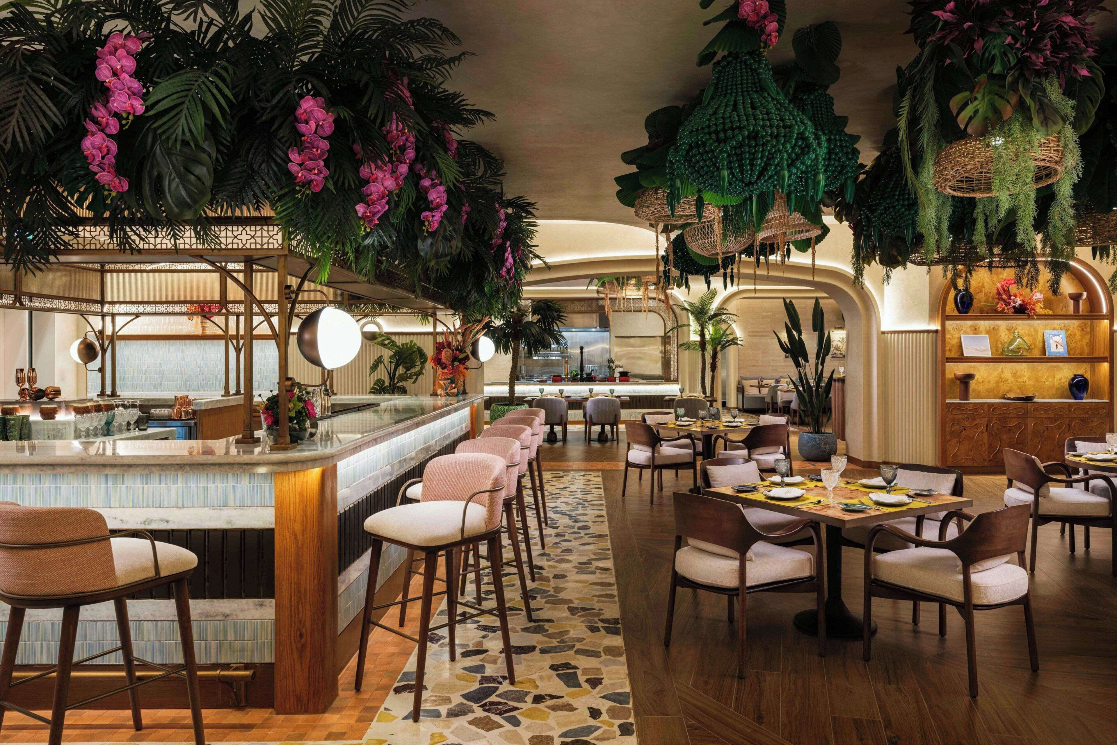 A restaurant with a bar area, multiple seating options, and lush indoor plants.