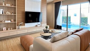 Un salon moderne doté d’un téléviseur à écran plat, d’étagères en bois, d’un canapé et offrant une vue sur une piscine.