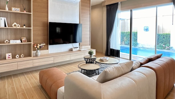 Un salón moderno con televisión de pantalla plana, estanterías de madera, un sofá y vistas a una piscina.