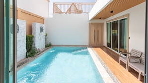 Una piscina con muelle de madera y puerta de cristal que da a un patio cubierto.