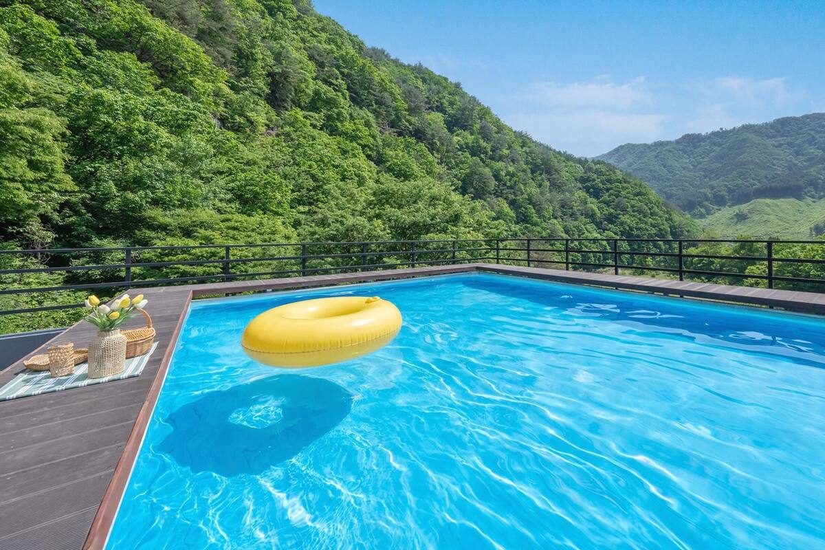 Une piscine avec un flotteur jaune, entourée d’une terrasse en bois et d’une rambarde en métal, qui offre une vue sur une vallée verdoyante.