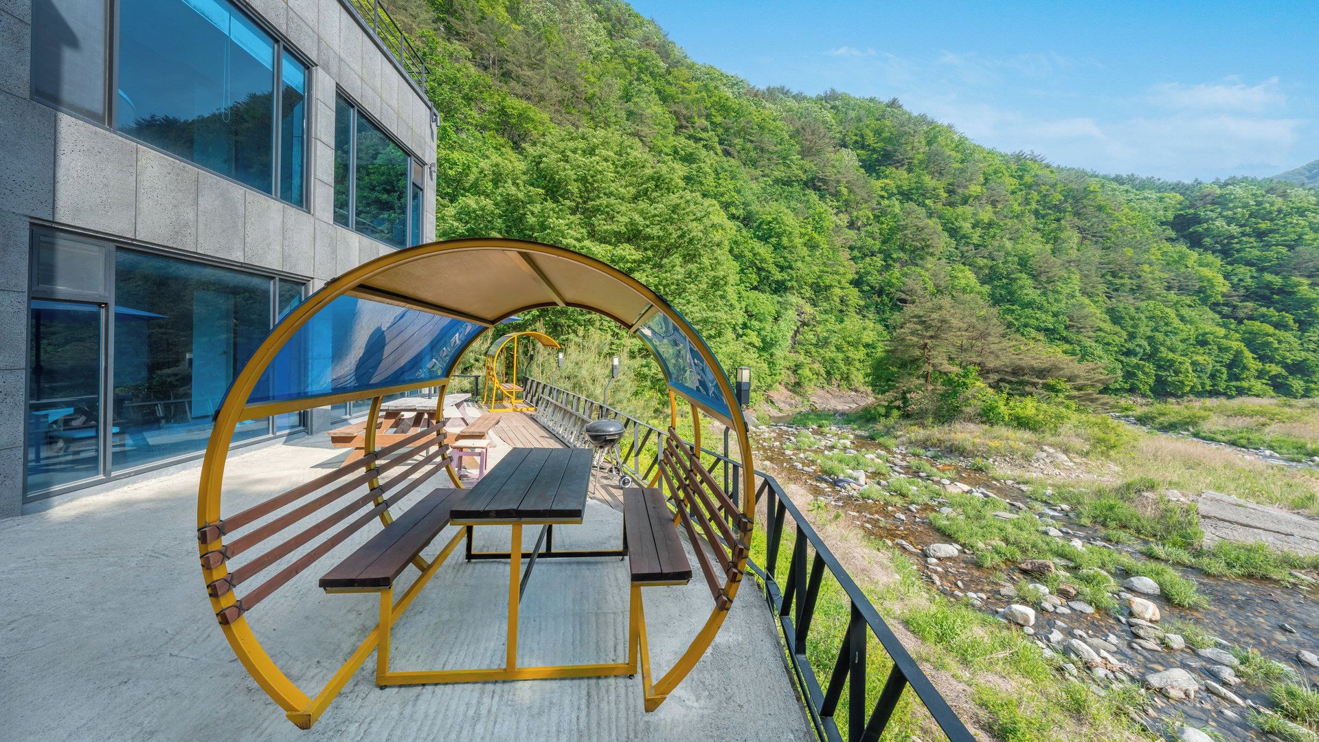 An outdoor deck with picnic tables and a view of a river and forested hills.