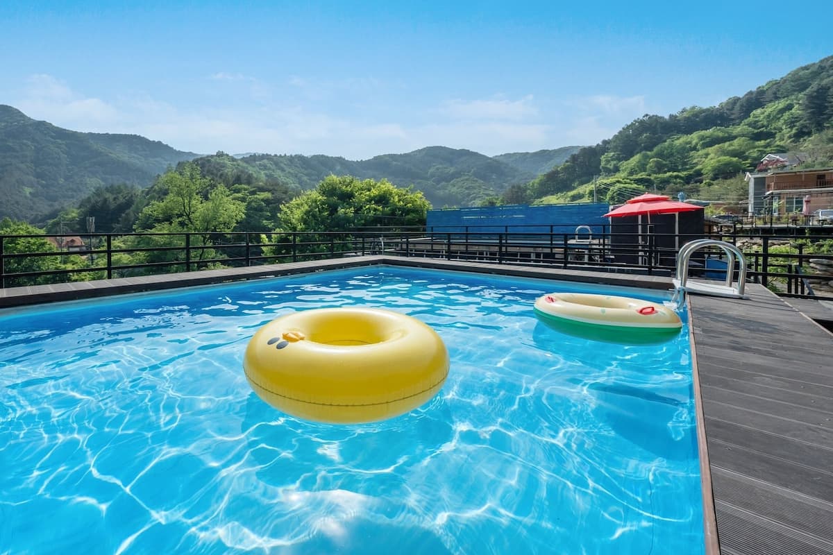 Une piscine avec deux bouées gonflables, entourée d’une terrasse en bois et d’une rambarde en métal.
