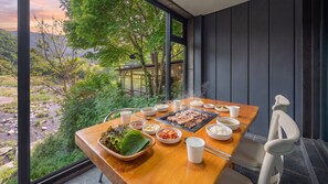 Une table à manger dressée avec différents plats et un barbecue, donnant sur un paysage naturel.