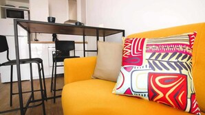 A modern living room with a yellow sofa, a black metal table, and a colorful patterned pillow.