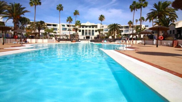 A swimming pool with palm trees and a building in the background.