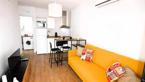 A compact living space with a kitchenette, a sofa with colorful pillows, and a dining area.