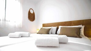 A neatly made bed with white linens and a wooden headboard, accompanied by rolled towels and a decorative wall hanging.