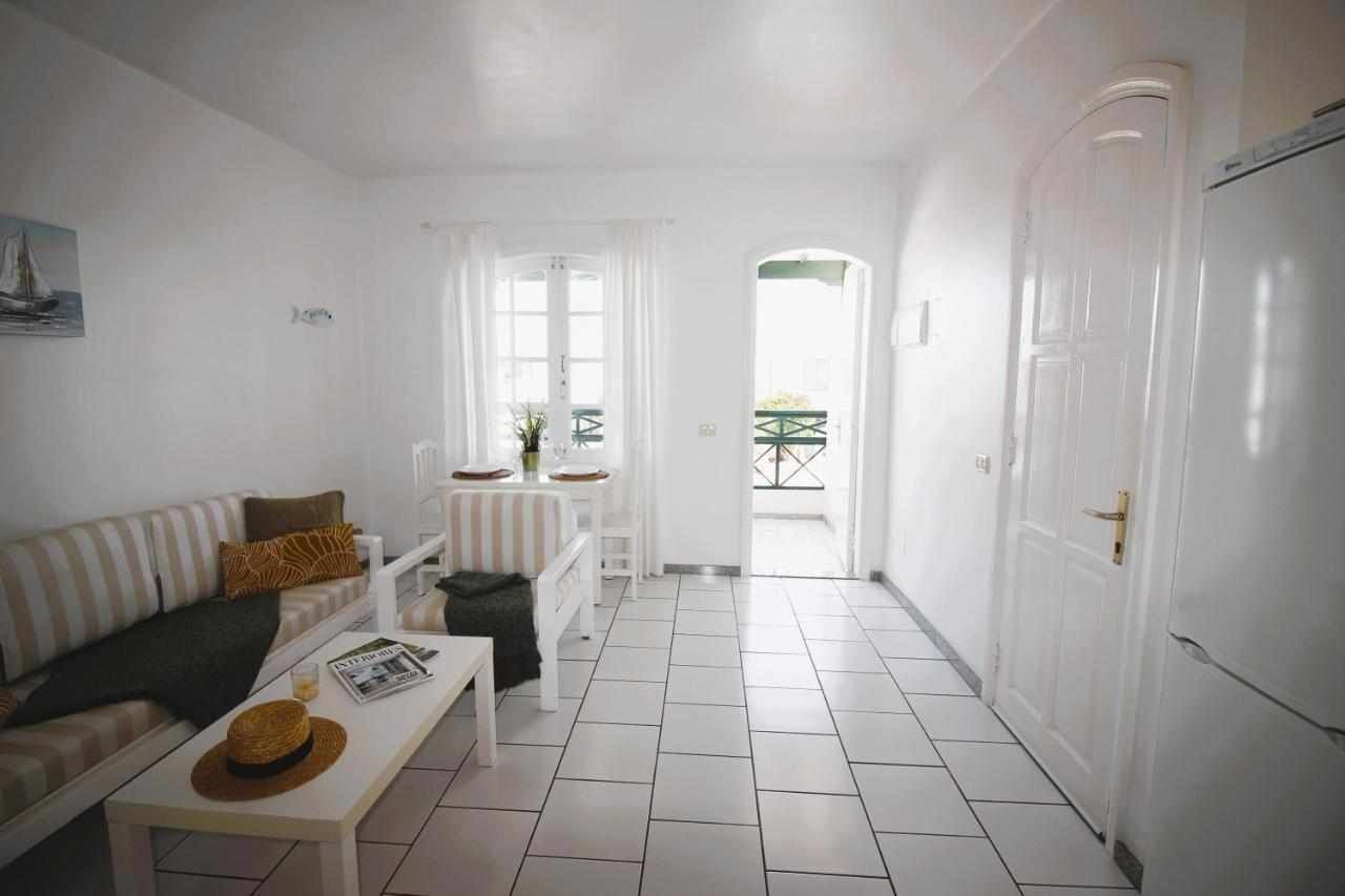 A bright, white room with a striped sofa, a small table, and a door leading to an outdoor area.