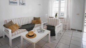A modern, minimalist living room with a striped sofa, a small coffee table, and a dining area with a white table and chairs. - Nautic Apartment in Puerto del Carmen (Puerto Del Carmen)