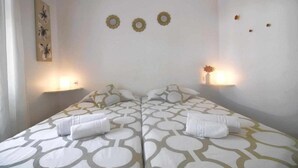 A double room with two beds, each with a patterned bedspread and pillows. There are wall-mounted lights and a small wall decoration. - Nautic Apartment in Puerto del Carmen (Puerto Del Carmen)