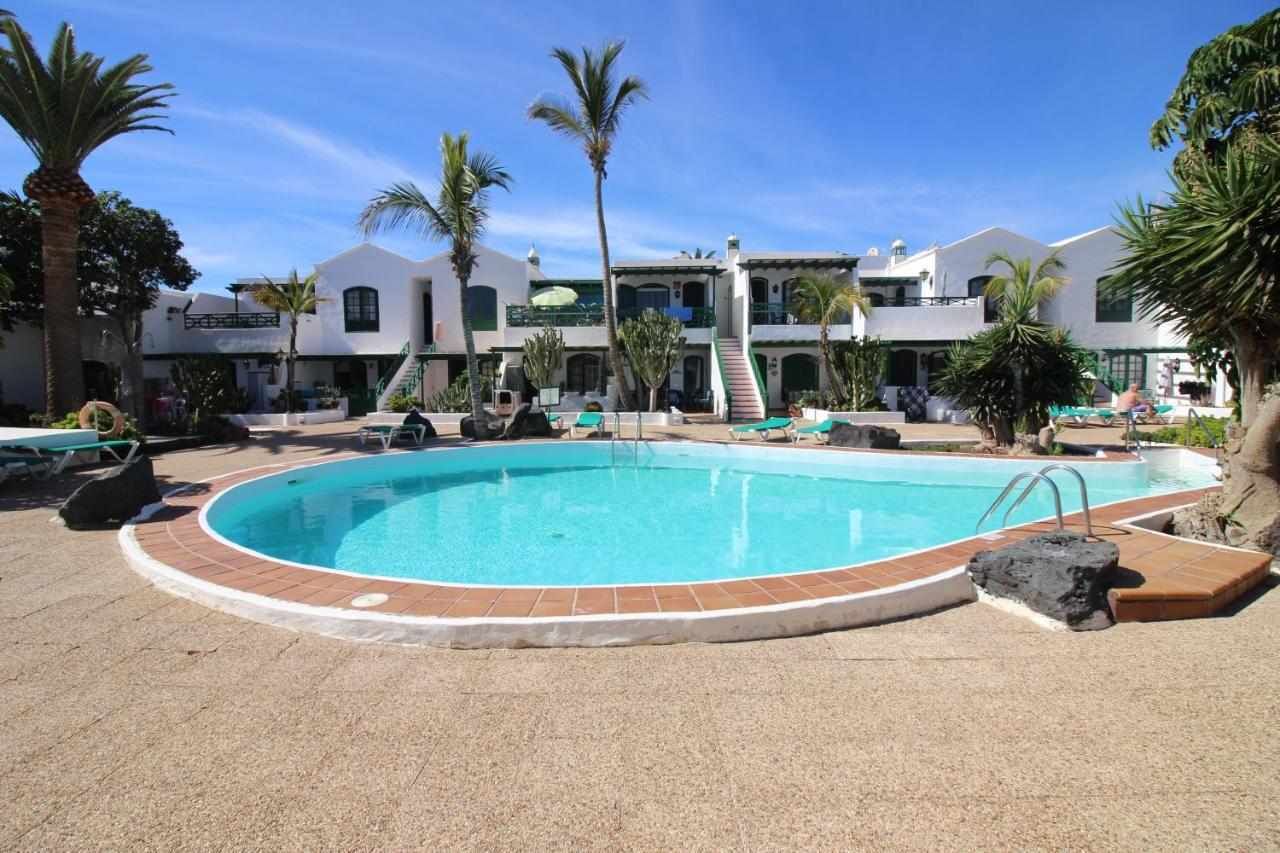 Una piscina con borde de azulejos, rodeada de palmeras y sillas de descanso.