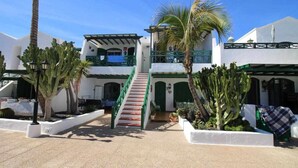 A courtyard with a staircase leading to a second-floor balcony, surrounded by cacti and palm trees. - Nautic Apartment in Puerto del Carmen (Puerto Del Carmen)