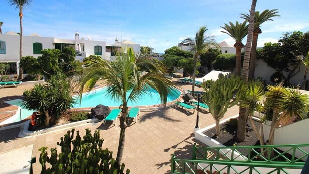 A pool area with lounge chairs, palm trees, and a clear blue sky. - Nautic Apartment in Puerto del Carmen (Puerto Del Carmen)