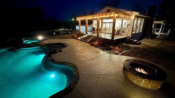 A swimming pool with a curved design, a fire pit, and a covered patio area with outdoor seating.