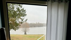 A bathroom with a bathtub, a window with a view of a lake, and a shelf with toiletries.