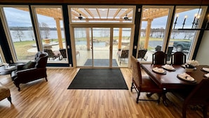 A spacious room with a large sliding glass door leading to an outdoor patio area. Inside, there is a wooden dining table set for four, a leather armchair, and a sofa.