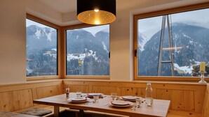 A dining area with a wooden table and benches, large windows with a mountain view, and a hanging light fixture. - Home Dachsbau by Interhome (See)