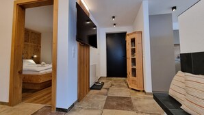 A hallway with a wooden wardrobe, a television mounted on the wall, a black door, and a cabinet with glass doors. - Home Dachsbau by Interhome (See)