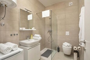 Ein modernes Badezimmer mit einer gläsernen Duschkabine, einem Waschbecken mit Spiegel darüber und ordentlich gefalteten Handtüchern auf der Ablagefläche.