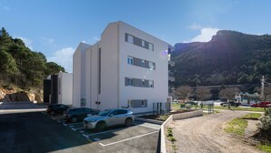 A modern building with a parking lot and a mountainous backdrop. - Sea-View Balcony Apt Lady Laura, Plomin, Croatia (Plomin)