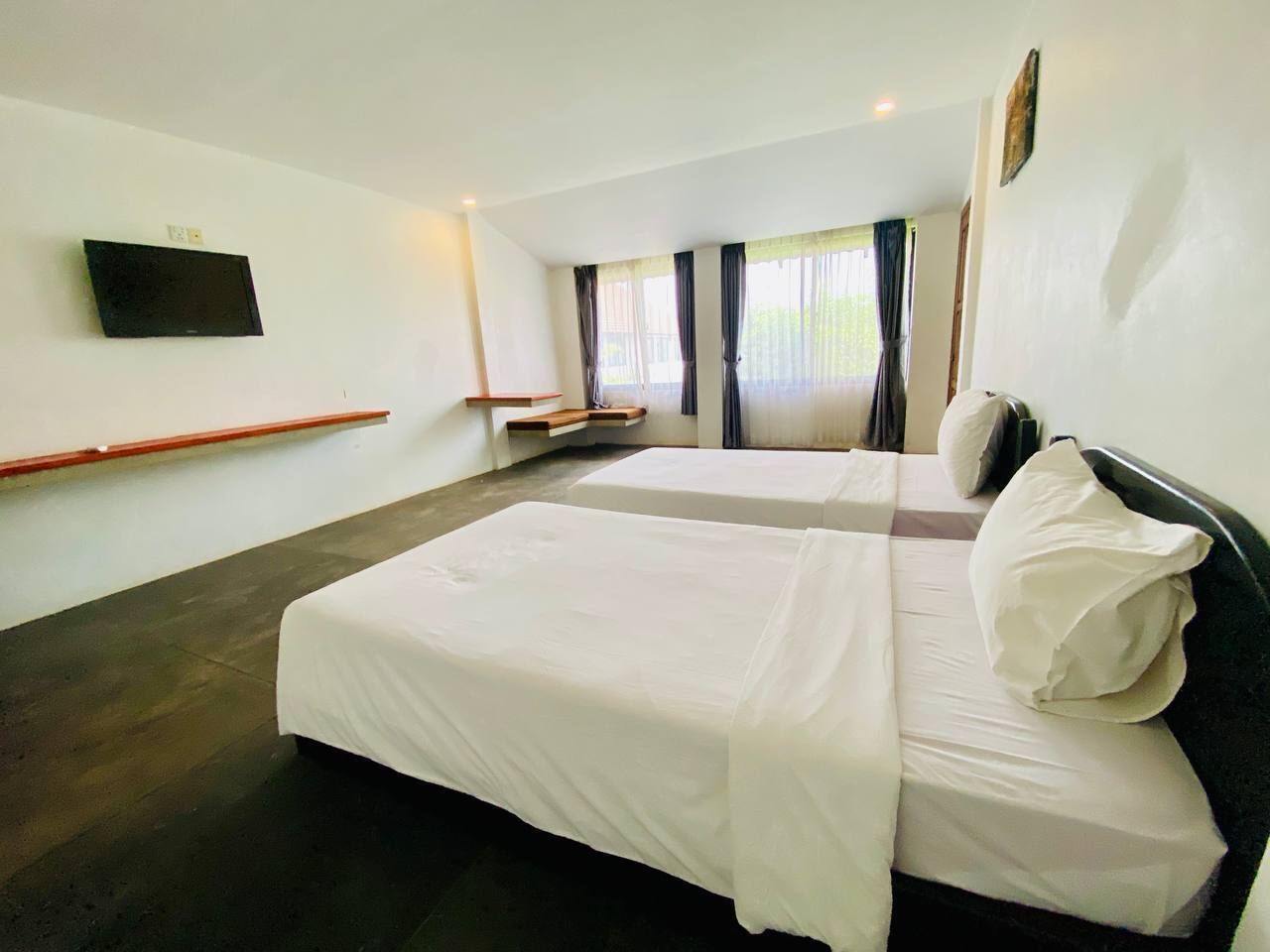 A hotel room with two beds, a flat-screen TV mounted on the wall, and a window with curtains.