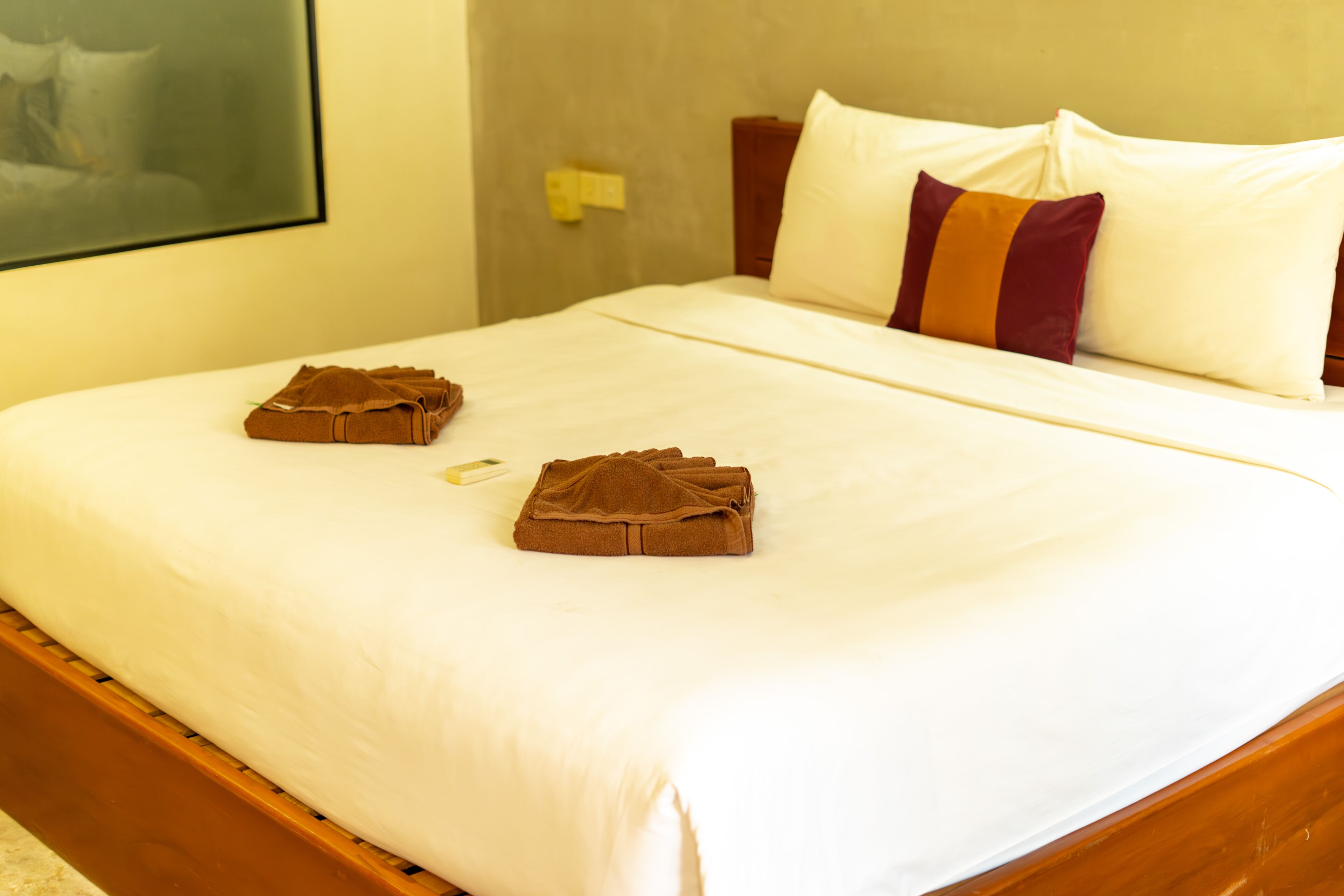 A neatly made bed with white sheets and two brown towels folded on the bed.