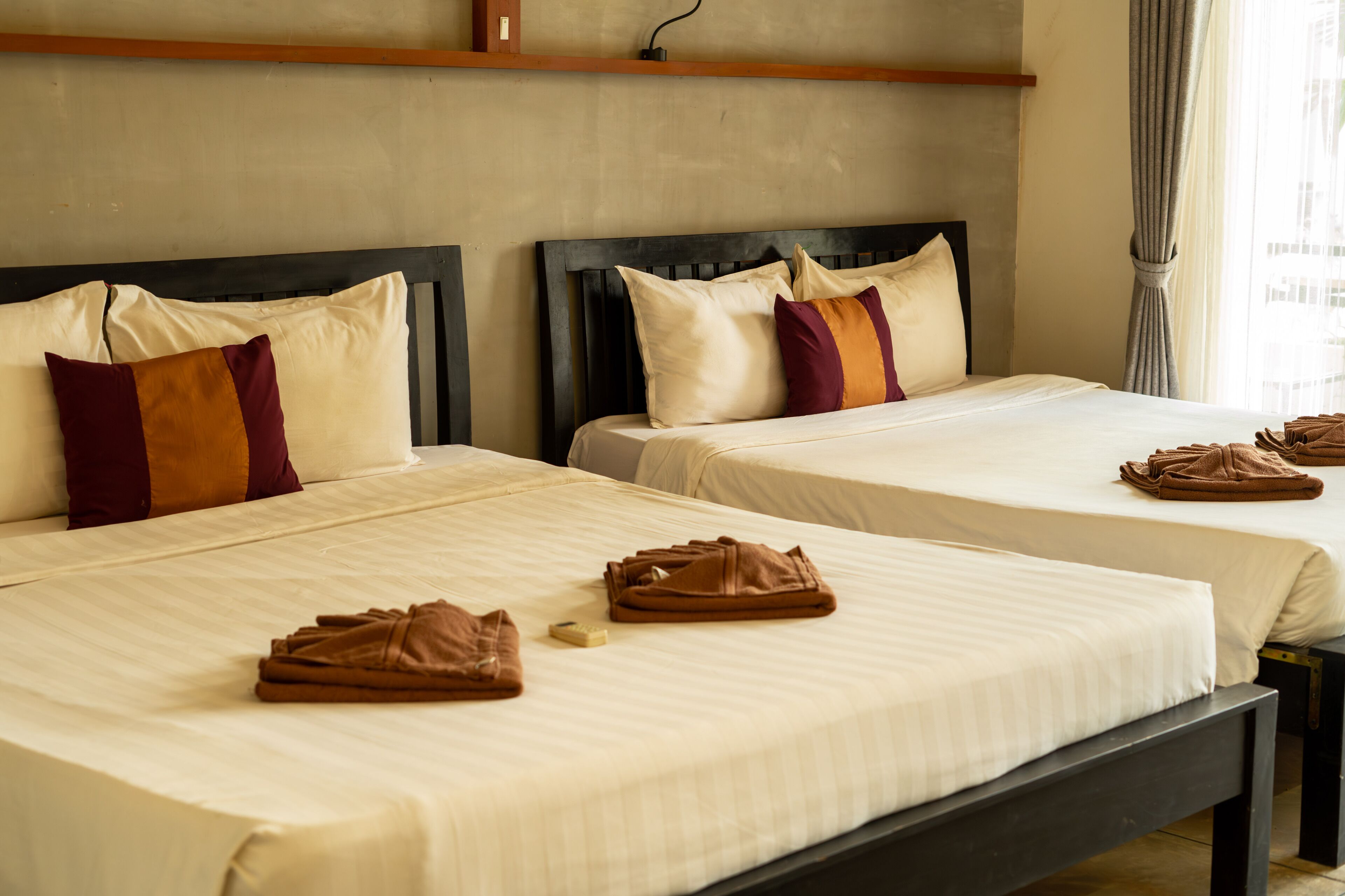 A hotel room with two beds, each with a headboard, pillows, and folded towels.