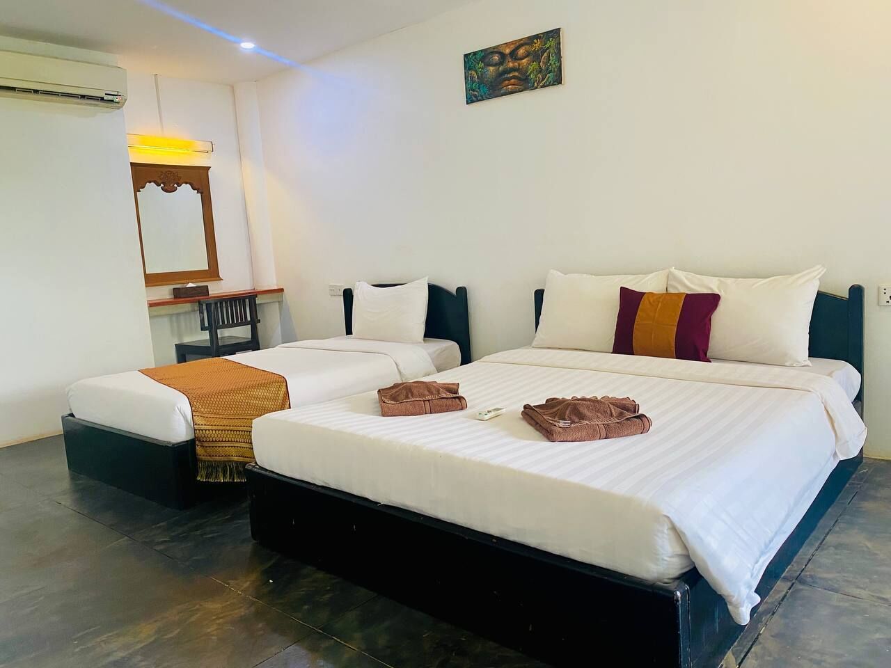 Habitación de hotel con dos camas, un espejo, una silla y aire acondicionado instalado en la pared.