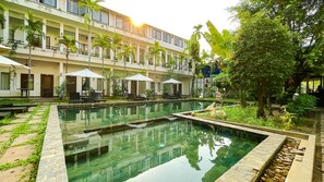 A pool area with lounge chairs and umbrellas, surrounded by a building with balconies and plants. - Lok Taneuy Residence (Siem Reap)