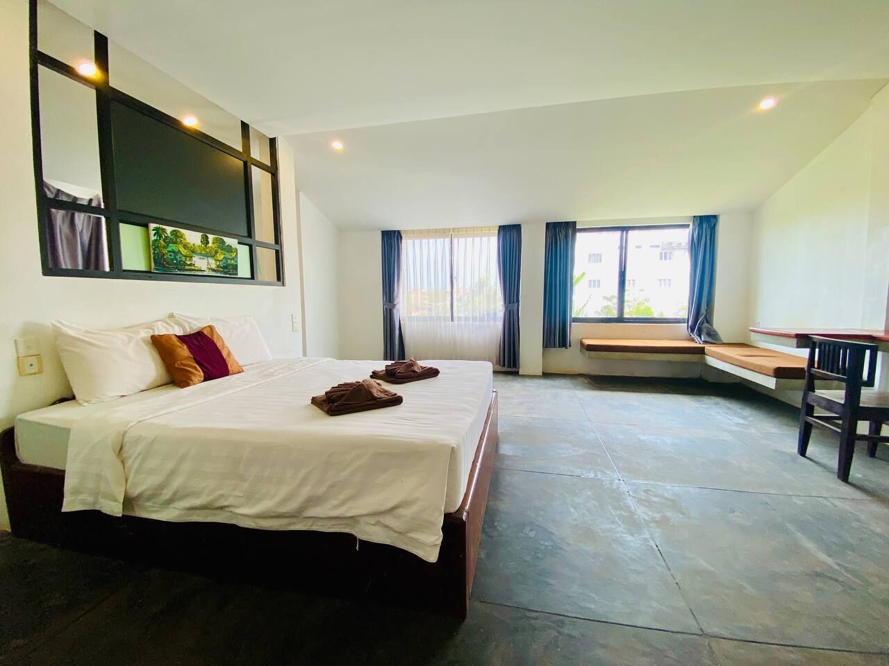 A hotel room with a large bed, a bench by the window, and a desk.