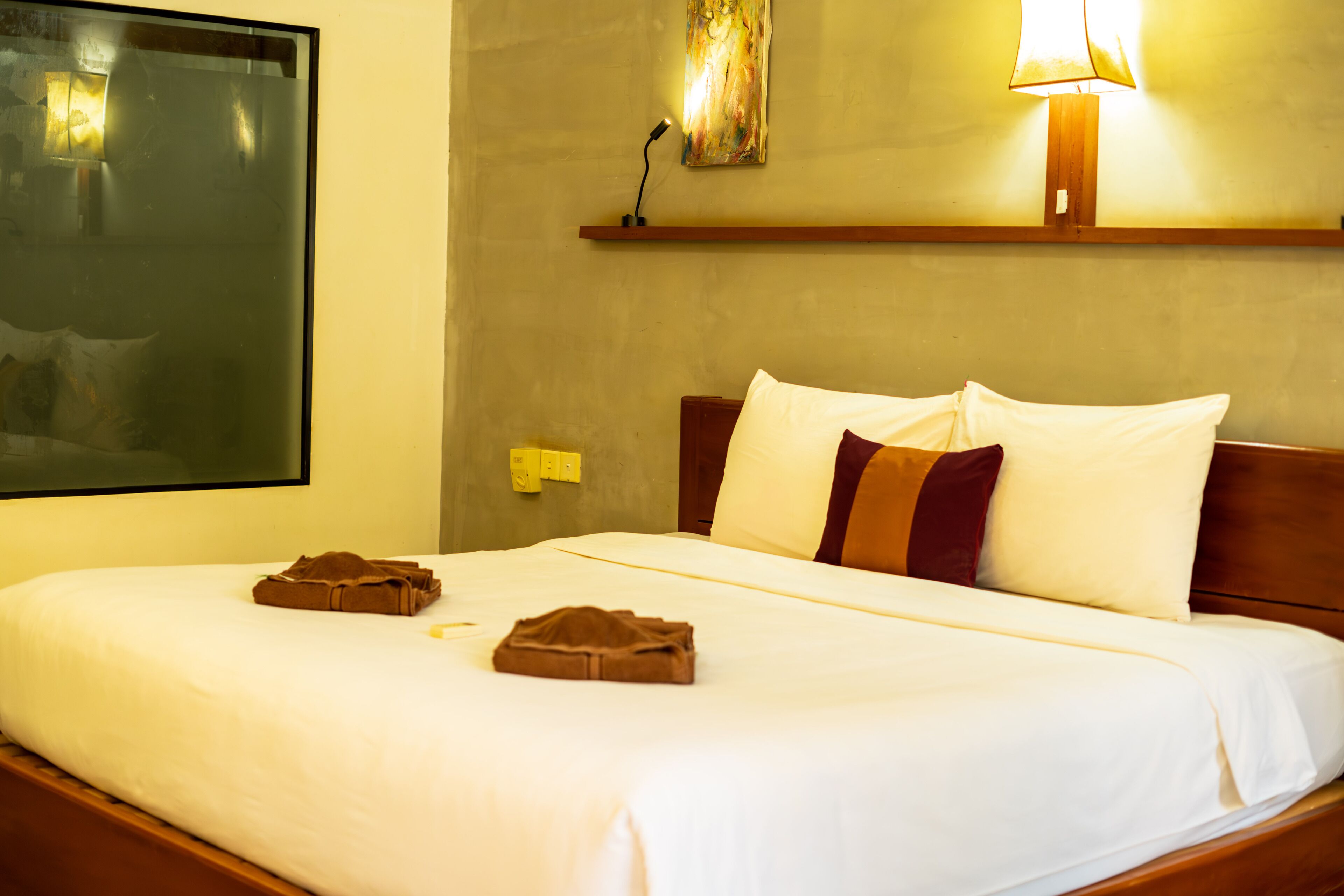 A hotel room with a large bed, a nightstand, a lamp, and a painting on the wall.