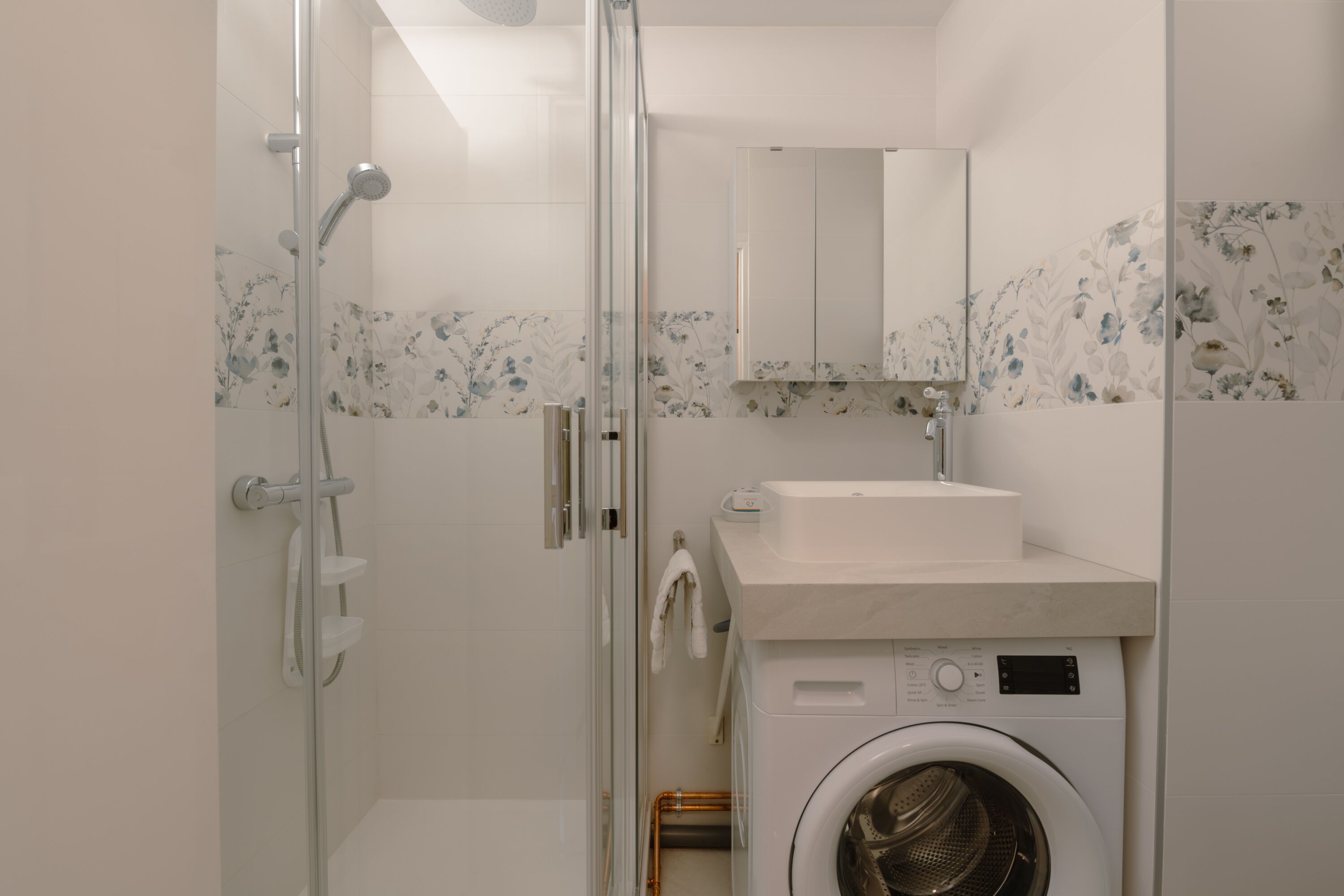 Une petite salle de bain dotée d’une douche à parois de verre, d’un lave-linge et d’un lavabo avec un miroir au-dessus.