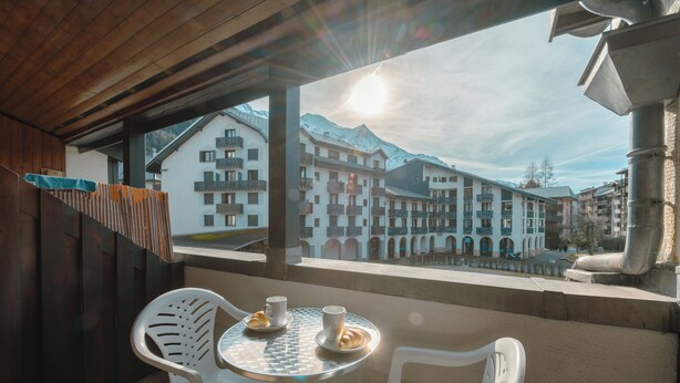 A balcony with a table and chairs, overlooking a town with traditional buildings and a mountain in the background. - Cham Sud Genévrier104 sleeps 2 next Aiguille du Midi, Chamonix, France (Chamonix)