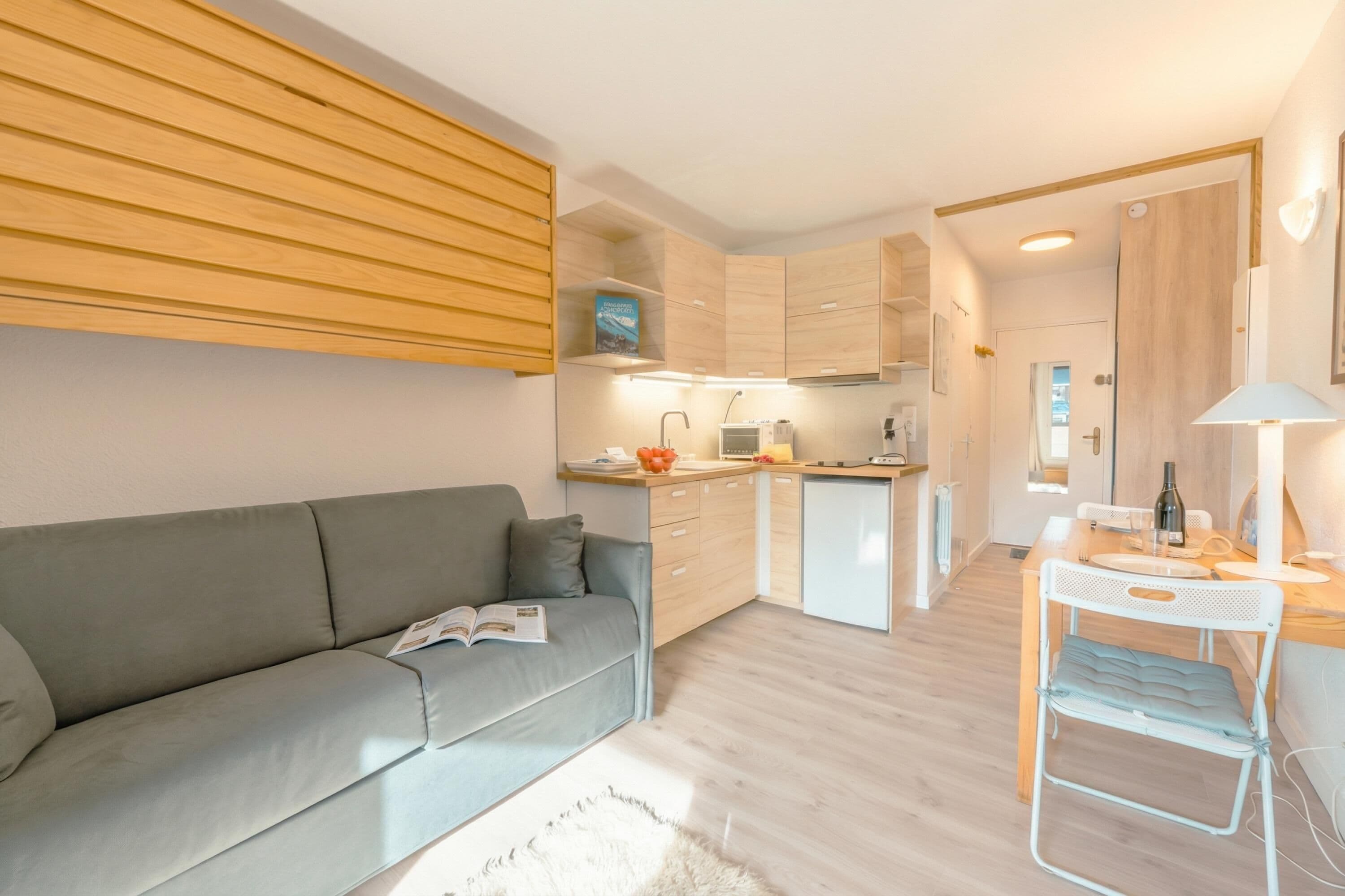A modern apartment with a grey sofa, a small dining table, and a kitchenette.