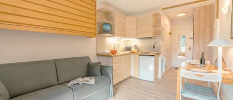 A modern apartment with a grey sofa, a small dining table, and a kitchenette.