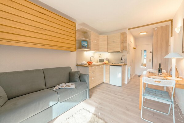 A modern apartment with a grey sofa, a small dining table, and a kitchenette.