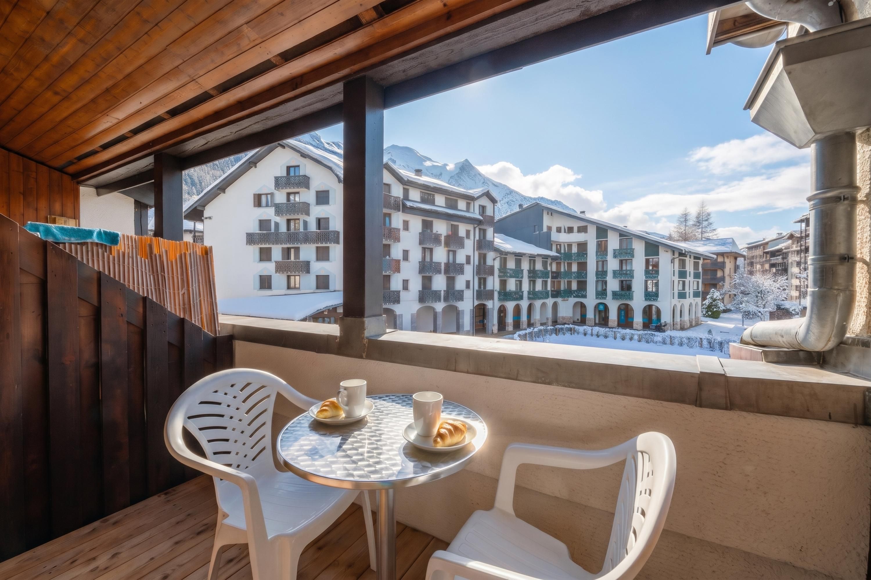 A balcony with a table and chairs, overlooking a snowy mountain landscape with buildings.