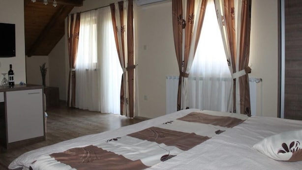 A bedroom with a bed, curtains, a radiator, and a small table with a bottle. - Agrotourism Vinia (Bjelovar)
