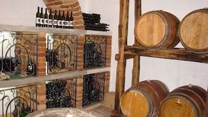 A wine cellar with wooden barrels and metal racks holding wine bottles. - Agrotourism Vinia (Bjelovar)